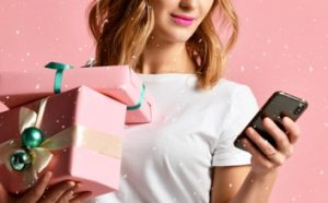 Woman using her phone and holding two gift boxes