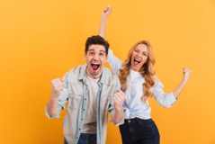 Excited couple smiling and laughing in front of a yellow background