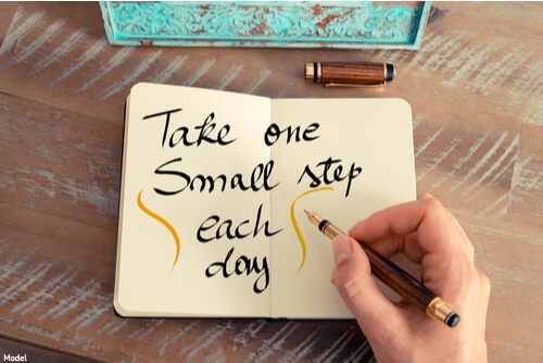 Person writing in a journal 'take one small step each day'