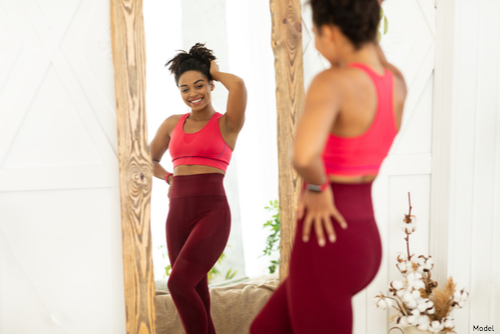 Confident woman in activewear looks at herself in the mirror and smiles