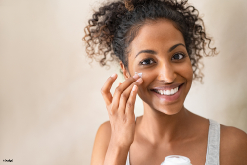 Joyful woman smiling while applying skin care products to her face