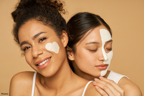 Two women with skin care products on their faces smiling