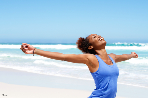 Confident woman at the beach with outstretched arms smiling