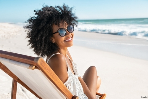 Woman with black hair by the shore lounging in a beach chair and smiling