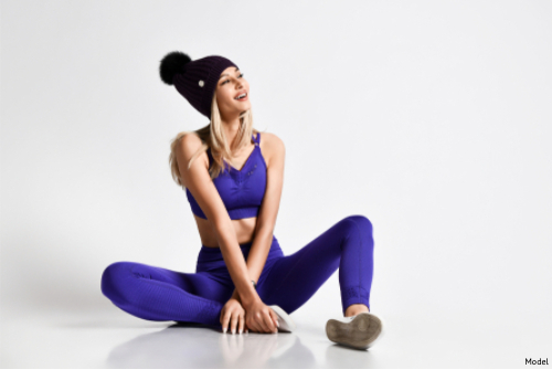 Woman in purple activewear and a winter hat sitting on the floor smiling