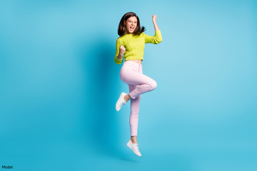 Confident, empowered woman in a yellow sweater and pink jeans jumping up in celebration