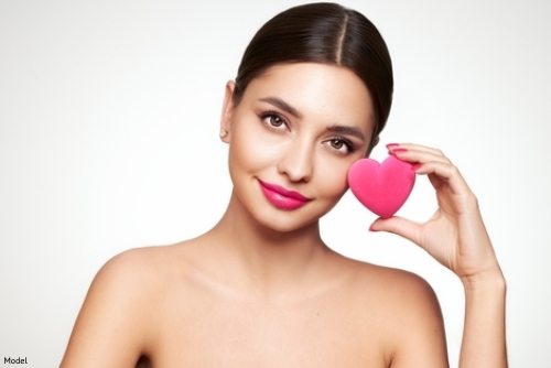 Woman with clear, bright skin wearing pink lipstick and holding a pink heart up to her face