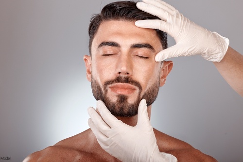 Masculine man with a beard having his face examined by gloved hands