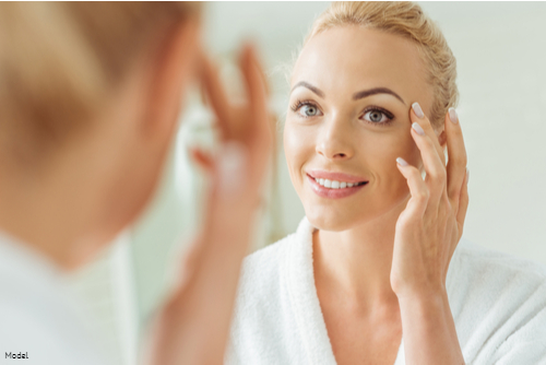 Mature woman with blonde hair looking at her skin in the mirror