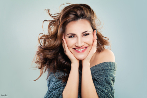Woman with long brown hair cupping her face in her hands and smiling