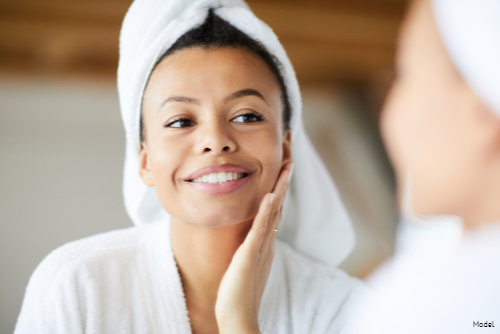 Joyful woman in a bathrobe touching her skin in the mirror