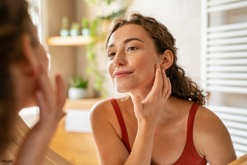 Confident woman with brown curly hair looking at her skin in the mirror