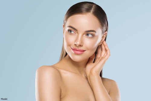 woman feeling cheekbones with sky blue background