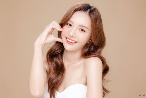 Confident, smiling woman with natural skin holding her hand up to her face in the shape of a heart