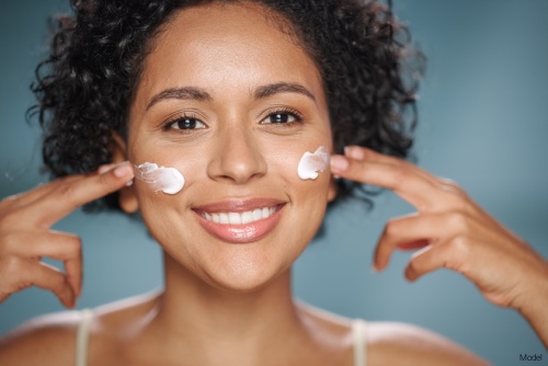 Cheerful woman with clear skin applying sunscreen to her cheeks