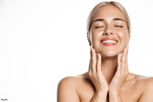 Tranquil woman with clear, bright skin smiling and gently touching her face