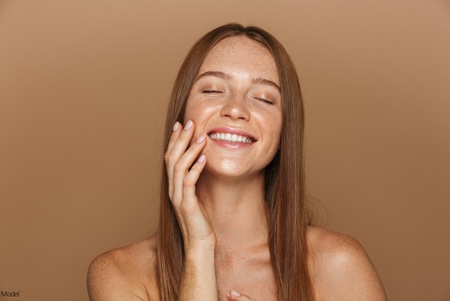 Confident woman smiling with her eyes closed and gently touching her face