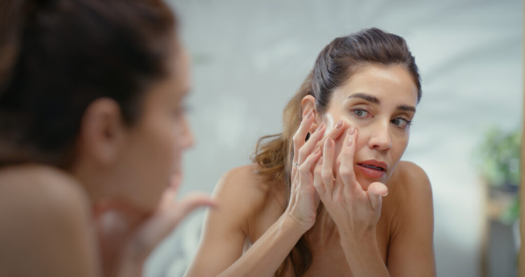 Woman with adult acne looking in the mirror
